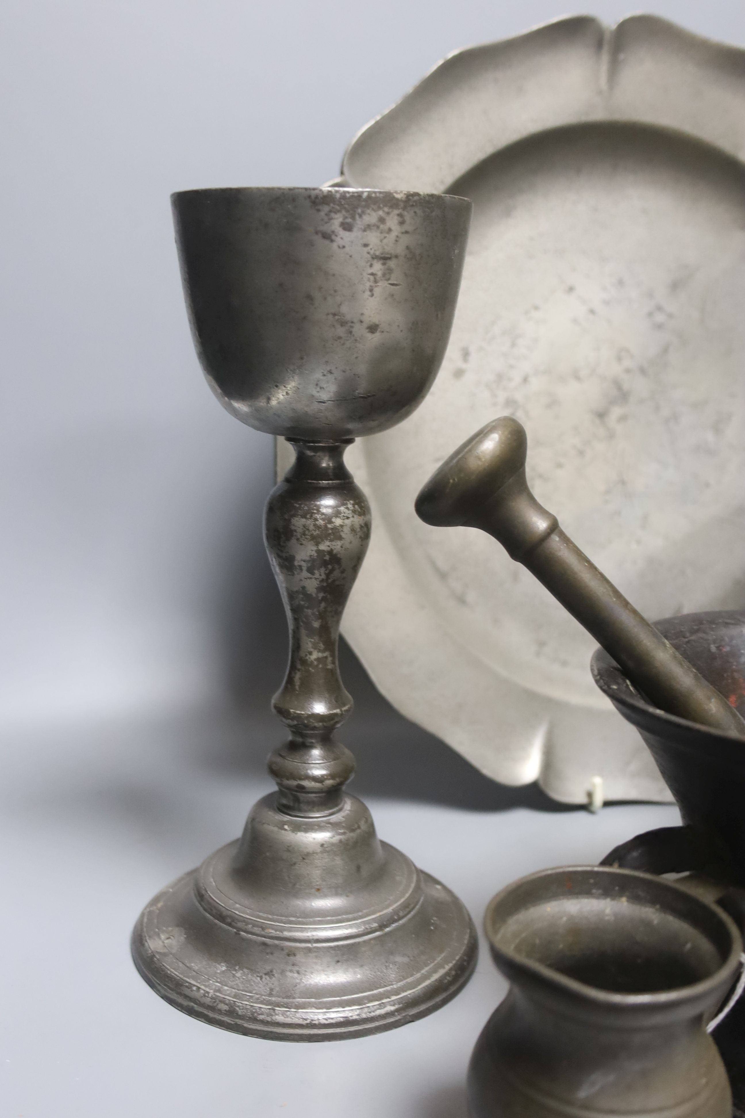 A pewter pedestal bowl, a barbed and crested dish, three other items of pewter and a 17th/18th century bronze pestle and mortar